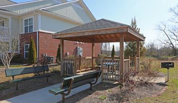 Gazebo with a wooden roof is surrounded by benches and plants.